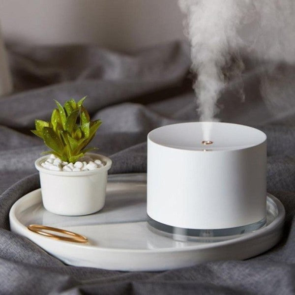 White BEAU Glow Humidifier & Ambient Lamp emitting steam on a gray tray with a small plant, all on a gray fabric background.