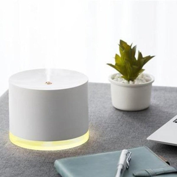 White Beau Glow Humidifier & Ambient Lamp with glowing base on a gray surface next to a small plant and notebook.