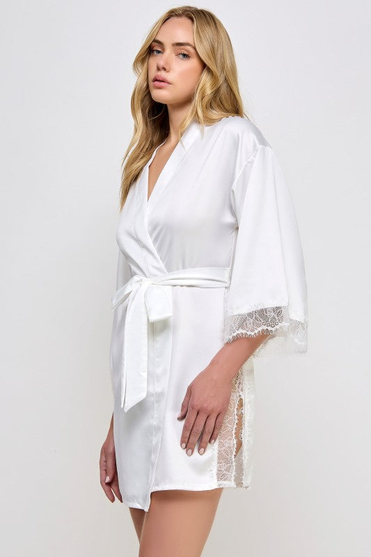 Woman wearing a white Beau satin robe with lace trim on a plain background