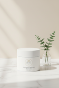 White jar of Beau Wellness & Beauty Clay mask for pores and blackheads with 'BEAU' branding next to clear glass vase with two steams of green leaves on a white marble background with a beige wall.