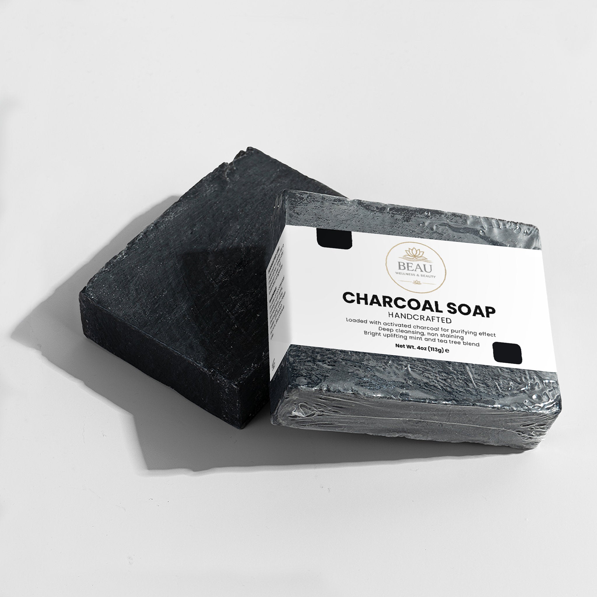 Two bars of handcrafted charcoal soap with a Beau Wellness & Beauty packaging label on a light gray background
