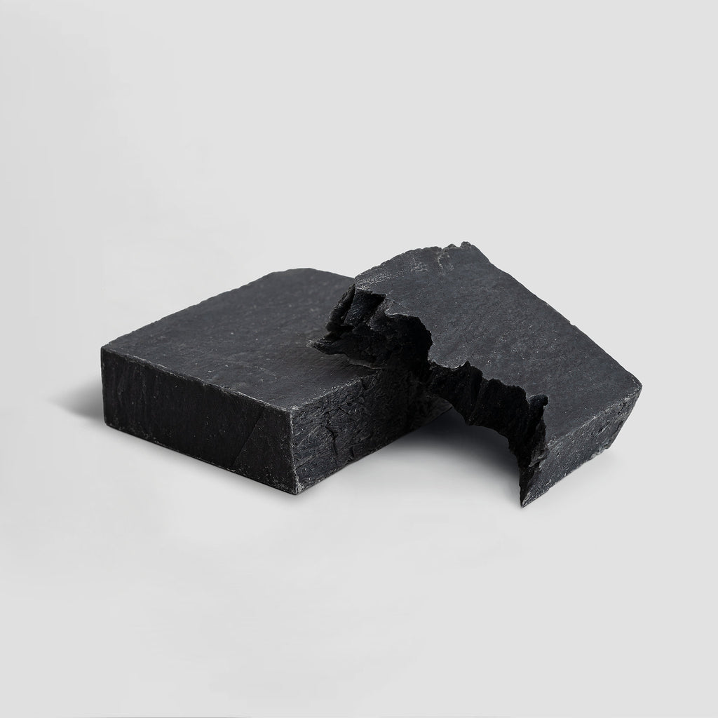 Two pieces of black charcoal soap on a light gray background