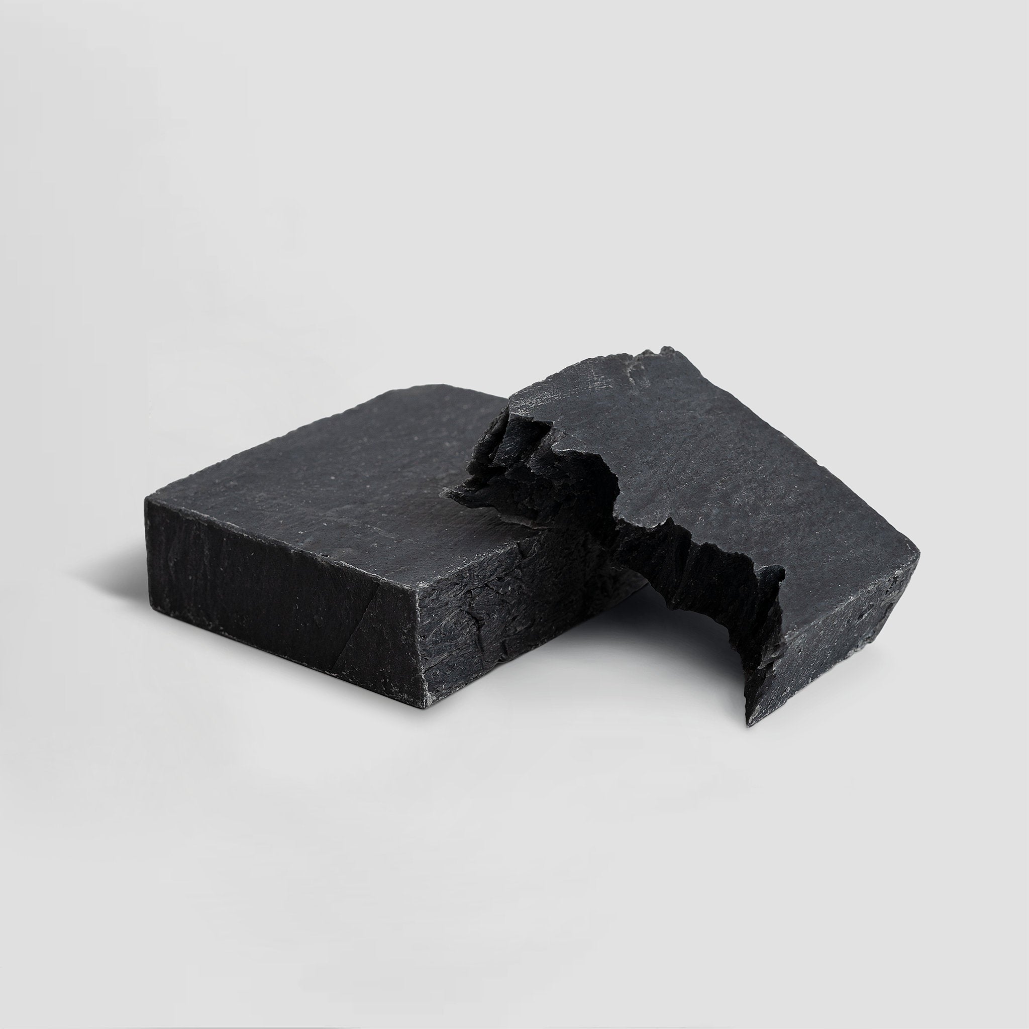 Two pieces of black charcoal soap on a light gray background