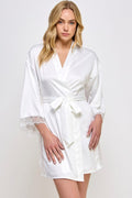Woman wearing a white satin robe with lace cuffs on a plain background