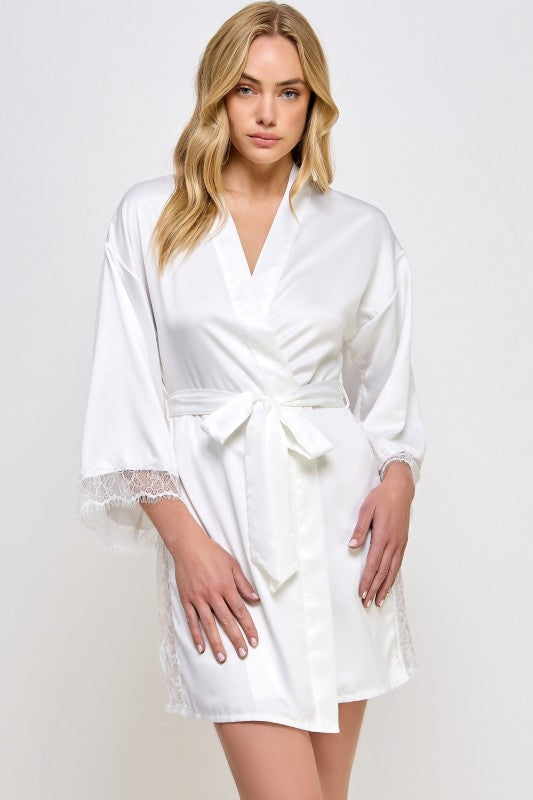 Woman wearing a white satin robe with lace cuffs on a plain background