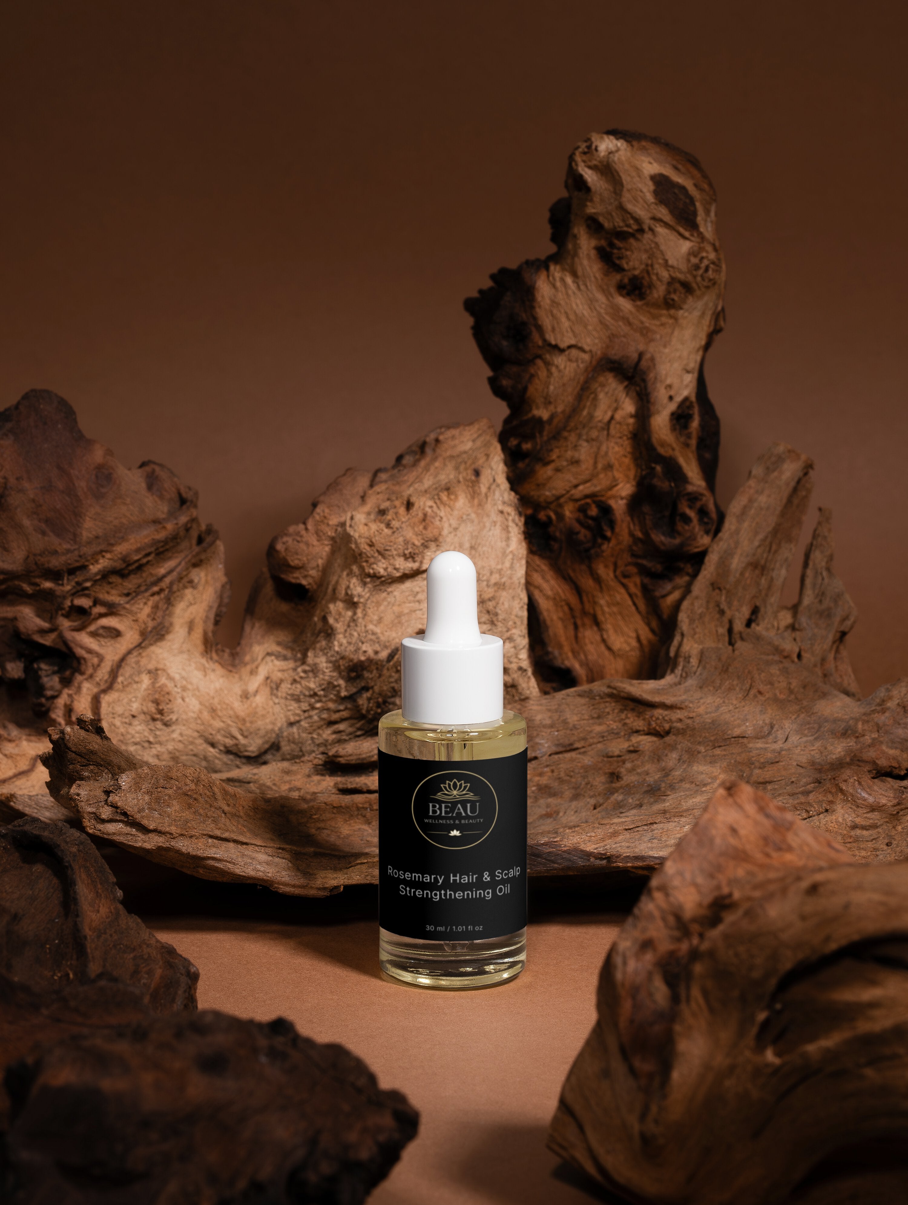 Beau House Rosemary Hair and Scalp Strengthening Oil in a clear glass dropper bottle in its luxury black and gold branded label in a wood theme background.