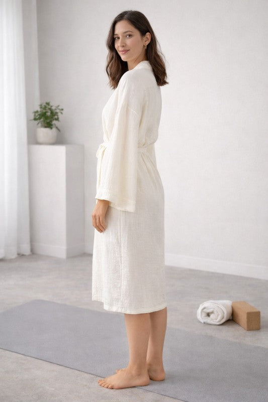 Woman in a white Cotton Muslin Wrap Robe standing on a yoga mat in a minimalistic room.