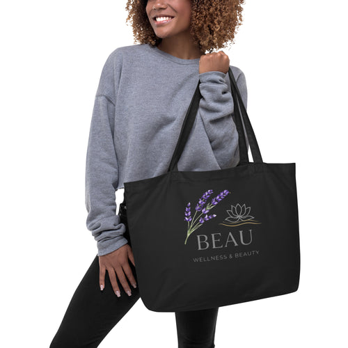 Woman holding Black Large Organic Market Tote bag featuring a printed lavender sprig, lotus flower logo, and the Beau Wellness & Beauty brand name.⁠
