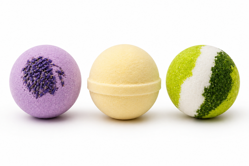 
Three handcrafted round bath bombs lined up on a white background: a purple lavender bomb with dried flower buds, a smooth pastel yellow lemongrass bomb, and a vibrant green and white eucalyptus bomb.
