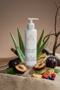 Beau Wellness & Beauty Clarifying Gel Cleanser bottle on a sandy surface with citrus fruits, plums, and aloe vera plant driftwood