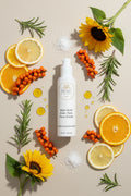 Beau Wellness & Beauty Kojic Acid Even Tone Face Cream with sunflowers, rosemary, orange and lemon slices in the background with a few drops of oil.