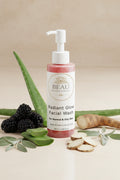Facial wash bottle labeled 'Radiant Glow Facial Wash' by BEAU Wellness & Beauty on a tan background with blackberries, burdock root , sage leaves and aloe vera.