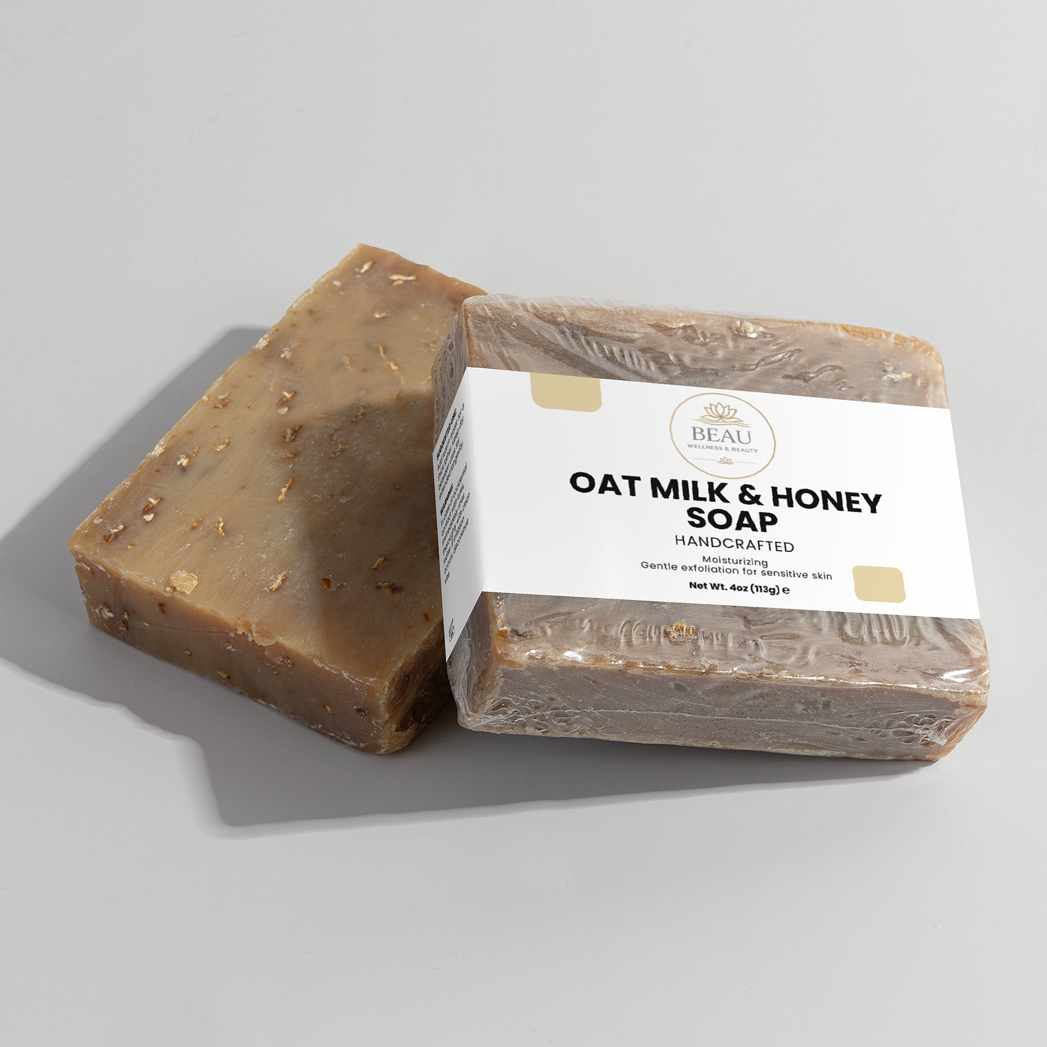 Two  handcrafted bars of oat milk and honey soap with a visible Beau Wellness & Beauty label on a light gray background