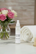 Bottle of skin rest face mist on a bathroom counter with a towel, soap, and scrubber in the background.